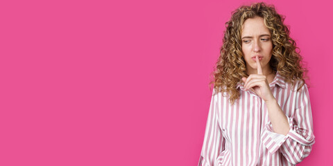 A young woman makes a gesture with her hands quietly, applying them to her lips.