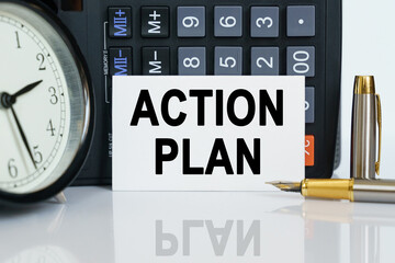 On the table there is a clock, a pen, a calculator and a business card on which the text is written - ACTION PLAN