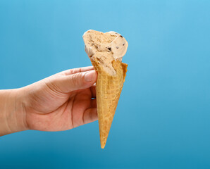 hand holding a half eaten milk tea flavor ice cream cone on a blue background horizontal composition