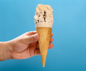 hand holding a milk tea flavor ice cream cone with a bite on a blue background horizontal composition