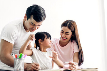 Portrait enjoy happy smiling love asian family father and mother with little asian girl learning and writing in book with pencil making homework at home.Education concept