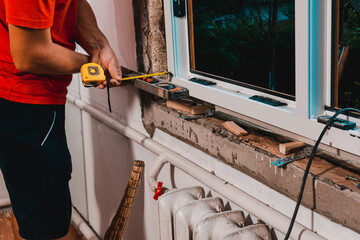 The man performs installation work with the window, for this he also uses a tape measure, measures...