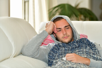 Close up of a young man looking sick lying on a sofa and covered with a blanket. Sickness and healthcare concept.