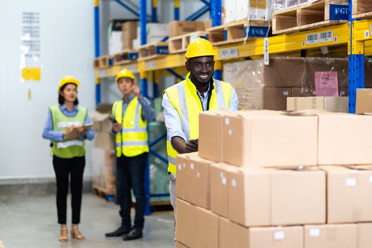 Black Male warehouse worker pulling a pallet truck. middle aged African American warehouse worker preparing a shipment in large warehouse distribution centre