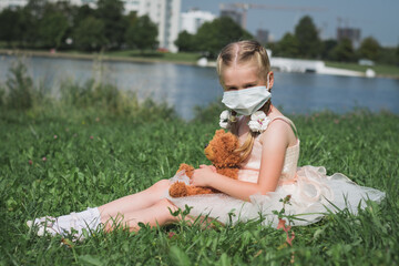 little girl in a protective mask and a teddy bear in her hands