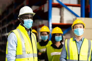 Warehouse worker in protective medical face mask working at large warehouse.  Many employees are working intently in the warehouse. Diversity peoples at work.