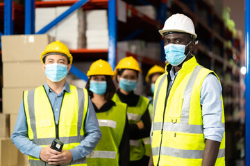 Warehouse worker in protective medical face mask working at large warehouse.  Many employees are working intently in the warehouse. Diversity peoples at work.