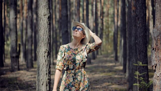 Beautiful Healthy Girl In Dress Walking In Greenwood.Carefree Female Exploring Spruce Forest In Sunny Time.Holiday Vacation Tourist Journey Trip In Warm Day.Active Woman In Hat Walking In Pine Forest.