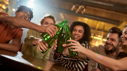 A group of happy friends in the bar watching sports match on TV together, drinking beer, clinking bottles and cheering for team. People, leisure, friendship and entertainment concept