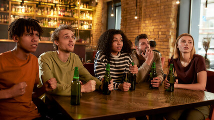 Friends looking worried while watching sports match on TV together, drinking beer and cheering for team in the bar. People, leisure, friendship and entertainment concept