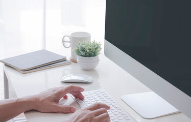 Cropped shot of man hands working with desktop computer while sitting at the table in comtemporary office room.