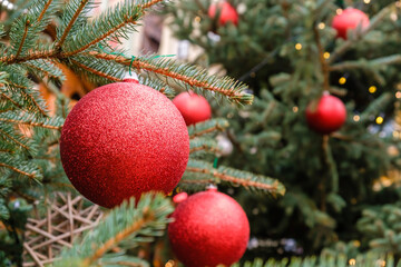 Obraz na płótnie Canvas Christmas Card. Closeup of Red New Year balls and garland on a branches of natural Christmas tree outdoors at sunny summer day.