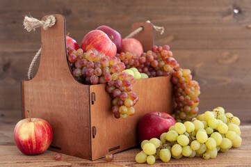 Fruit harvest. Ripe apples and grapes in a wooden box on a wooden background. Horizontal photo.