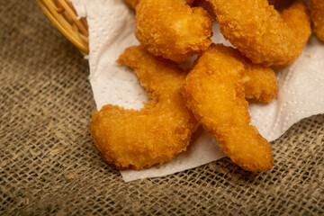 Atlantic shrimps fried in batter on a white paper napkin in a wicker basket. Close up.
