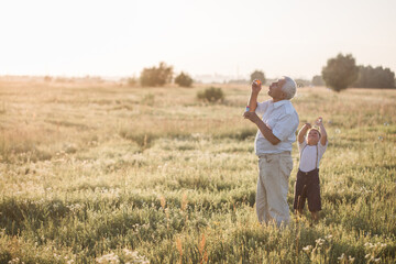 Naklejka na ściany i meble Happy senior man Grandfather with cute little boy grandson playing in field. Happy child with Grandfather playing outdoors