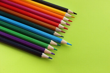 Colored pencils on yellow background. Lots of different colored pencils. Pencils are very sharp. Pencils lie in top corner. Blue pencil is pushed forward. Close-up. Copy space. Background. Flat lay
