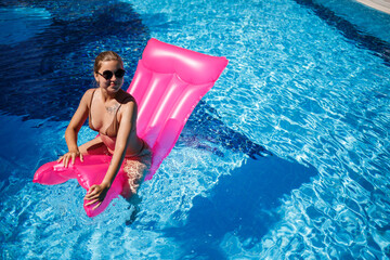 Sexy woman in sunglasses resting and sunbathing on a pink mattress in the pool. Young woman in...