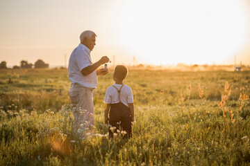 Fototapeta na wymiar Happy senior man Grandfather with cute little boy grandson playing in field. Happy child with Grandfather playing outdoors