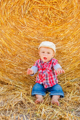 a Baby girl on a haystack happy on the field. Background with children a joyful childhood.