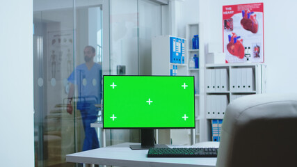 Computer with blank display in hospital cabinet and clinic personnel in the background. Desktop with copy space green screen mock up isolated available on medicine specialist in clinic cabinet.