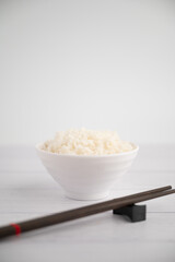 Thai steamed rice in a bowl with a spoon and black chopsticks placed on the side. On a white backdrop