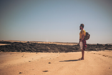 Standing man enjoying the desert traveling with a backpack - lonely people in the wild . men and outdoor nature traveling activity