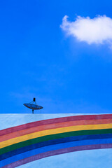 Satellite dish on top of the old building with rainbow stripes on building wall surface against blue sky in vertical frame