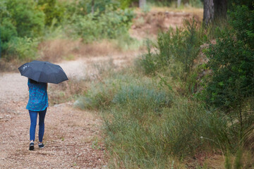 woman walking in the rain with black umbrella in rural setting