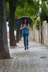 woman walking in the rain with black umbrella in rural setting