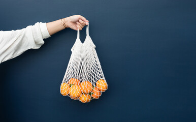 Female with fresh orange from garden in crochet bag.