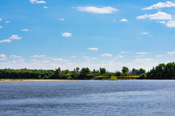 Photo of the river bend on the sunny day against clean blue sky. The steep Bank of the river is covered with dense forest.