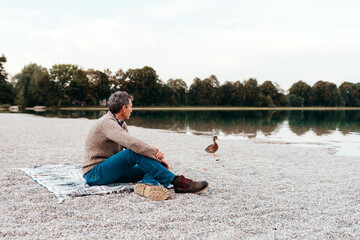 best ager man sitting at a lake watching a duck