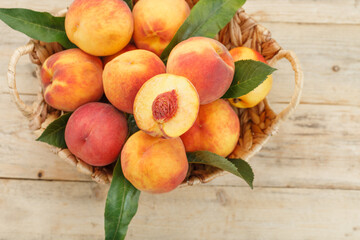 Naklejka na ściany i meble Peaches in a basket on a wooden background with a slice of sliced juicy peach with a stone.