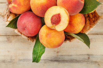 Fresh ripe peaches in a wicker basket on a wooden table, a slice of juicy peach with a stone.