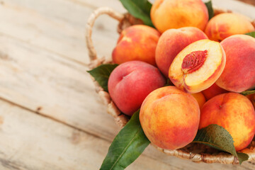 Fototapeta na wymiar Fresh ripe peaches in a wicker basket on a wooden table, a slice of juicy peach with a stone.