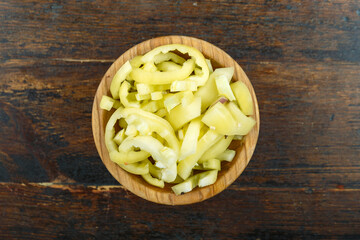 Sliced raw yellow peppers in a bowl on a wooden background. Vegetable, ingredient and staple food.