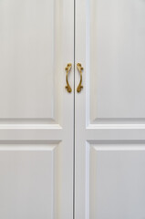 Classic white wardrobe with with ornamental golden handles close-up