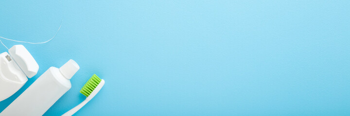 White tube of toothpaste, toothbrush with green bristles and container of dental floss on pastel...