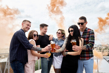 Group of friends drinking beer before festival at outdoors pub on roof, toasting and laughing, copy...