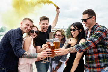 Group of friends drinking beer before festival at outdoors pub on roof, toasting and laughing, copy space. Friendship and celebration concept