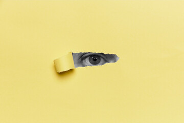 Image of human eye looking through hole in yellow paper sheet