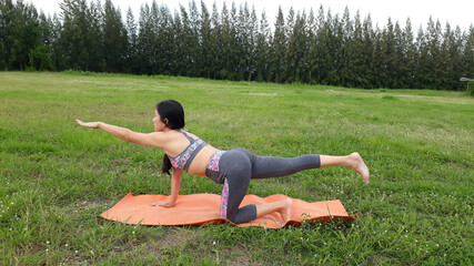 A woman wearing exercise clothes playing yoga on the mat outdoor afternoon.