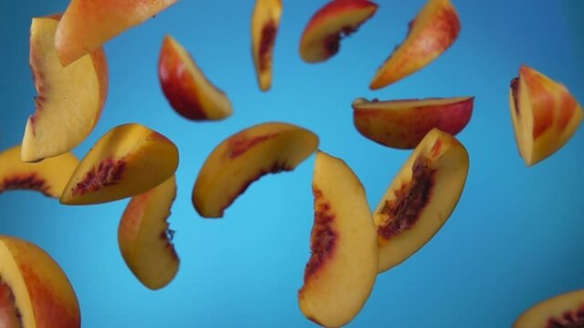 Slices of the fresh ripe peach are bouncing on the sky blue background in slow motion