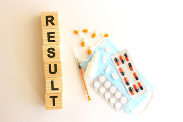 The words RESULT is made of wooden cubes on a white background with medical drugs and medical mask. Medical concept.
