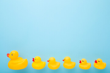 Yellow rubber mother duck and ducklings following one after other in row. Empty place for text on light blue table background. Pastel color. Top down view.