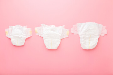 White soft baby diapers on light pink table background. Pastel color. Different sizes. Closeup. Top...