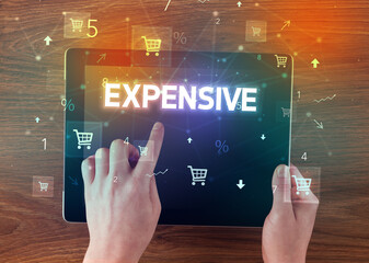 Close-up of a hand holding tablet with EXPENSIVE inscription, online shopping concept