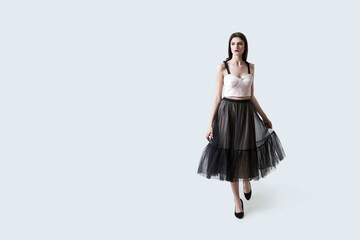 Young beautiful brunette girl in waving dark box pleated midi skirt posing in studio. Woman dancing or making a step.