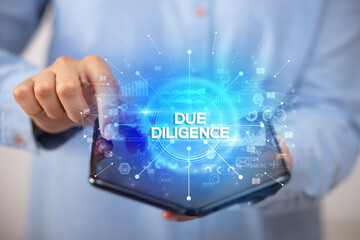 Naklejka na ściany i meble Businessman holding a foldable smartphone with DUE DILIGENCE inscription, new business concept