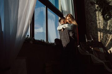 Romantic happy young couple enjoying time together sitting on the windowsill with blue sky outside the window. Pretty young smiling girl with closed eyes hugging her boyfriend .